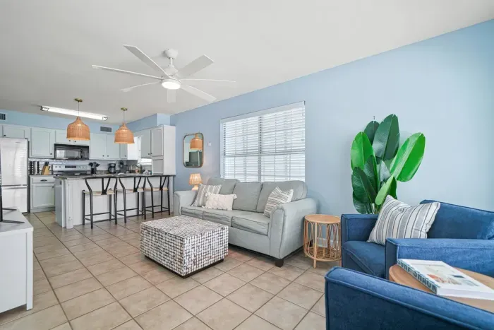 Open-concept main living area featuring a comfortable sofa and accent chairs, ceiling fan, and abundant natural light. Seamlessly connected to the fully equipped kitchen and bar seating—perfect for gathering, relaxing, and entertaining.