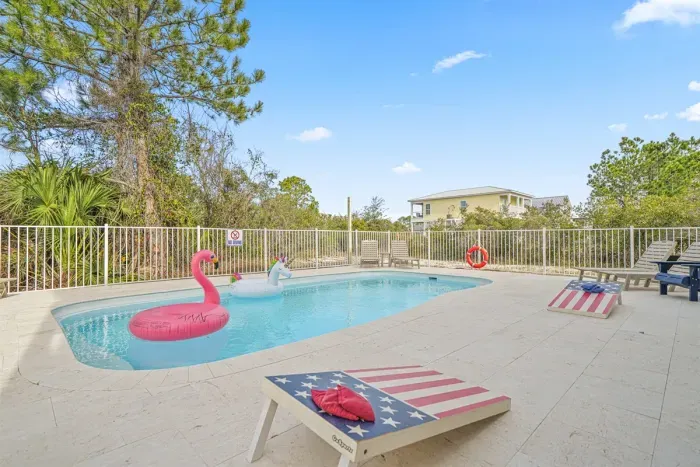 Sunny shared pool area with loungers, cornhole boards, and plenty of deck space to relax. Fully fenced for safety and shared with Unit A—perfect for cooling off after a beach day,