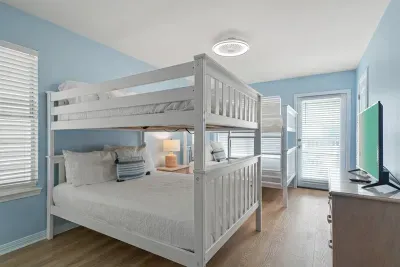 Bright bunk room featuring two queen-over-queen bunk beds, ideal for families or groups. Includes a TV, ample natural light, and direct access to a private ensuite bathroom—comfortable, functional, and thoughtfully designed for shared stays.