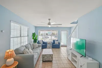 Bright and inviting main-level living area featuring comfortable seating, smart TV, ceiling fan, and large windows that fill the space with natural light—perfect for relaxing after a beach day or gathering with family and friends.