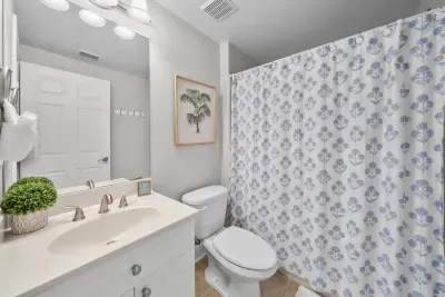 A bright bath with a vanity, a toilet and a patterned shower curtain for the tub and shower combo. Soaps and fresh towels are stocked for you.