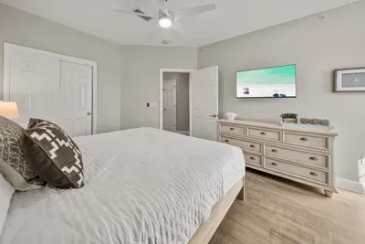 A roomy bedroom with a wall-mounted TV, a dresser and double closet doors. Plenty of space for suitcases without the clutter.