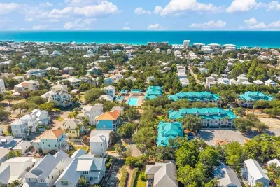 Blue Mountain Beach from above, with the Gulf on the horizon and the teal-roofed village a few steps from the sand. This is the quieter middle of 30A.