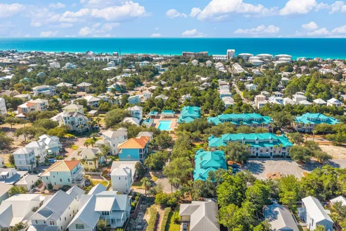 Blue Mountain Beach from above, with the Gulf on the horizon and the teal-roofed village a few steps from the sand. This is the quieter middle of 30A.