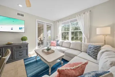 Sunny living room with an L-shaped sofa, a wall-mounted TV and a coffee table for game night. It opens to the kitchen and the patio, so the whole group stays together.