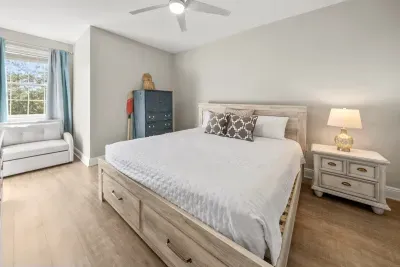 A comfortable bedroom with a ceiling fan, a bed with storage drawers underneath and a window that lets in the morning light.