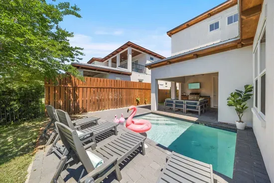 Sun-drenched afternoons by the pool — the heated pool, loungers, outdoor kitchen, and master balcony above make the backyard hard to leave.