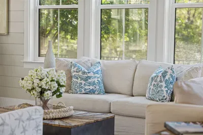The coastal sofa and floor-to-ceiling windows create a living room you'll actually want to stay in — bright, airy, and overlooking the trees.