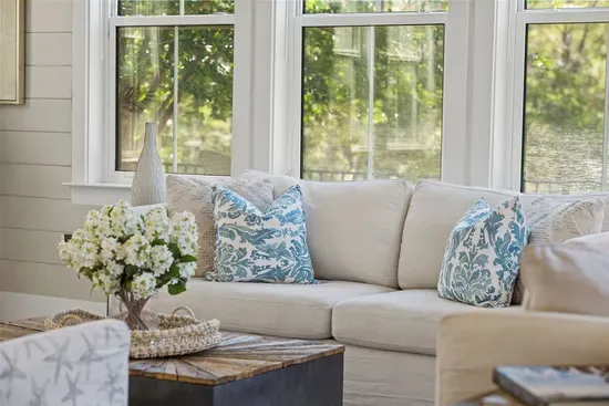The coastal sofa and floor-to-ceiling windows create a living room you'll actually want to stay in — bright, airy, and overlooking the trees.