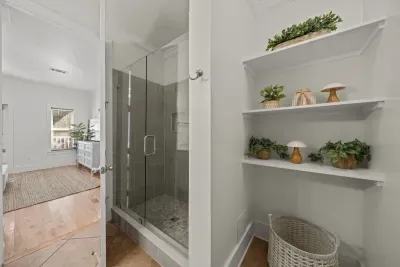 The master bath has a walk-in tile shower with glass doors and open shelves styled with beachy touches.