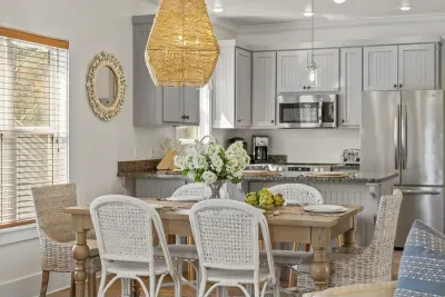 A bright dining area beside the kitchen, with a woven pendant light and white wicker chairs, makes breakfast a pleasure.