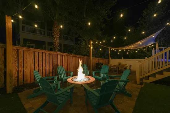 Private gas fire pit, surrounded by Adirondack seating and café lights—perfect for easy, worry-free evenings after the beach.