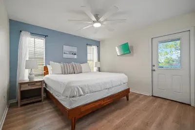 Bright and comfortable bedroom featuring a king bed, ceiling fan, wall-mounted TV, and private exterior balcony — ideal for relaxing after a day at the beach.