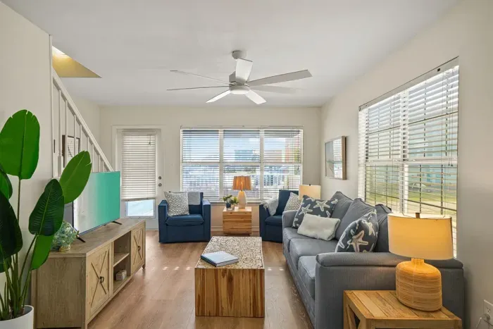 Bright and inviting living area with comfortable seating, large windows, ceiling fan, and smart TV—perfect for relaxing after a beach day.