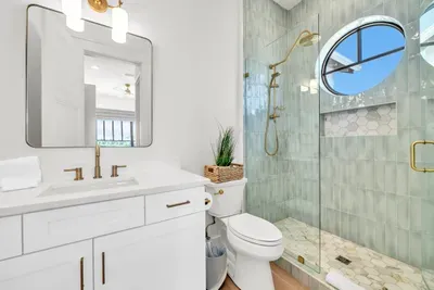 A porthole window over the shower is the kind of detail you remember. Full glass enclosure, warm gold fittings, and room to move.