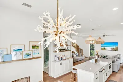 That coral chandelier is the showpiece of the main level, and it hangs right where the dining table, the coffee bar, and the kitchen all meet.