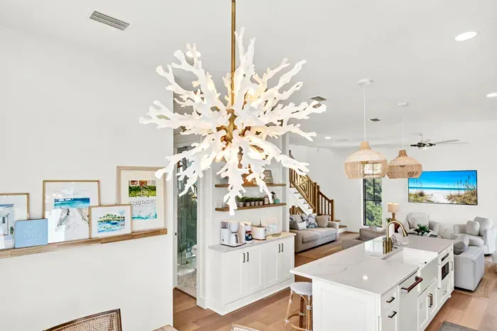 That coral chandelier is the showpiece of the main level, and it hangs right where the dining table, the coffee bar, and the kitchen all meet.
