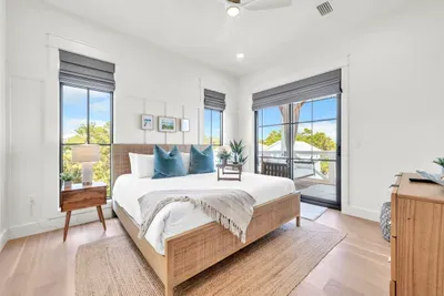Wake up here. The king bed sits between three shaded windows, and the door beside it opens onto a private balcony for the first cup of the day.