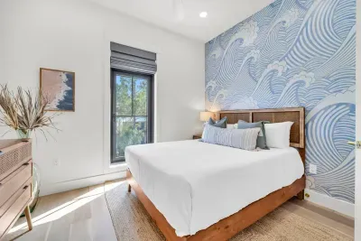 The wave wall says everything about where you are. Cane headboard, soft white linens, and quiet green views out the window.