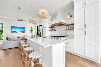White cabinetry to the ceiling, a vented hood over the gas range, and open shelves stocked for real cooking. The living room stays in view the whole time.