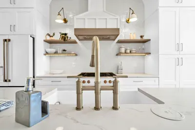 A bridge faucet over the farmhouse sink, a gas range under a custom hood, and sconces on the tile. The details a cook notices.