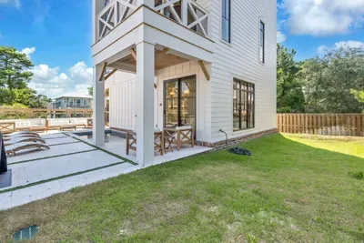 A real yard behind the pool deck, fenced and flat, with the covered patio and outdoor table at the edge of it. Bring the dog, there is room to run.
