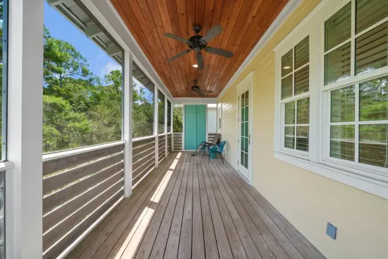 The covered second floor balcony runs the length of the house, with a ceiling fan and a view straight into the trees.