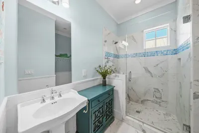 The vanity picks up the same sea glass tile that runs through the shower, with a walk-in glass enclosure alongside.