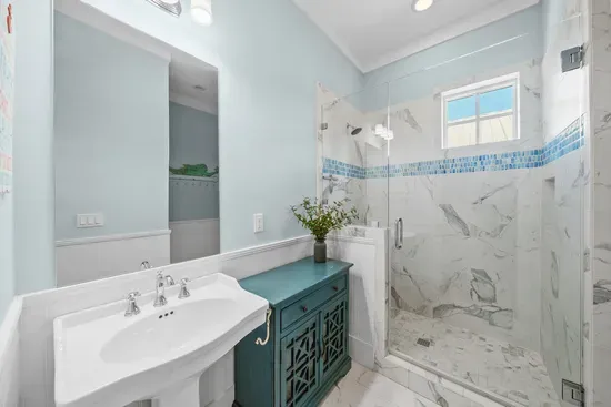 The vanity picks up the same sea glass tile that runs through the shower, with a walk-in glass enclosure alongside.