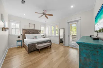 A bright guest bedroom with a ceiling fan, a smart TV, and windows on two walls.
