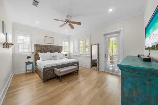 A bright guest bedroom with a ceiling fan, a smart TV, and windows on two walls.