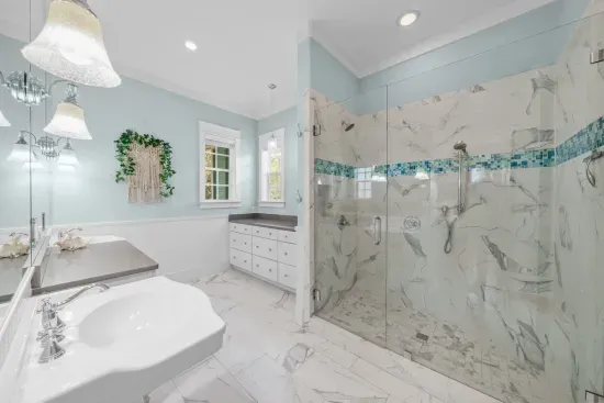 Marble underfoot and a glass walk-in shower with a ribbon of sea glass tile. Soft blue walls and good natural light.