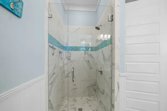 A tiled walk-in shower with a glass door and a sea glass accent band, shared by the two upstairs guest bedrooms.