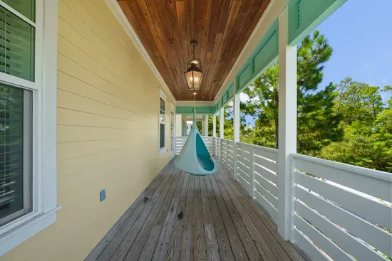 A hanging chair at the end of the covered porch, angled into the pines. Claim it early.