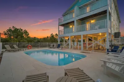 Twilight view of the heated saltwater pool with lounge seating, covered picnic tables, and soft evening lighting—perfect for winding down after a day at the beach.
