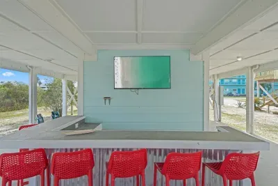 Covered outdoor bar area with seating and a wall-mounted TV—perfect for gathering, watching the game, or relaxing poolside after beach days.