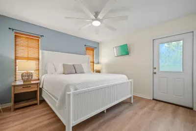 Unit A main bedroom featuring a king bed, private ensuite bathroom, and walk-out balcony with bay views. A bright, relaxing retreat with a wall-mounted TV and ceiling fan.