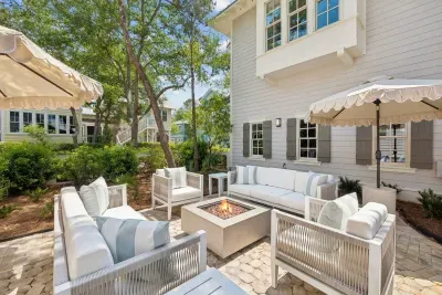 Your private outdoor living room — generous lounge seating circles a gas fire pit, all shaded by fringed umbrellas.