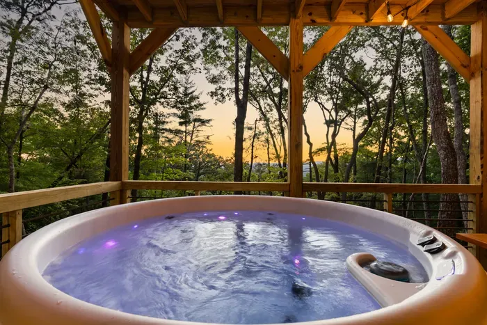 Private forest-view hot tub with a covered deck at sunset