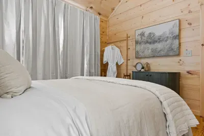 Cozy wood-paneled bedroom with plush linens and inviting cabin charm. Primary bedroom.