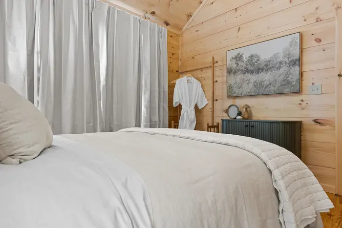 Cozy wood-paneled bedroom with plush linens and inviting cabin charm. Primary bedroom.