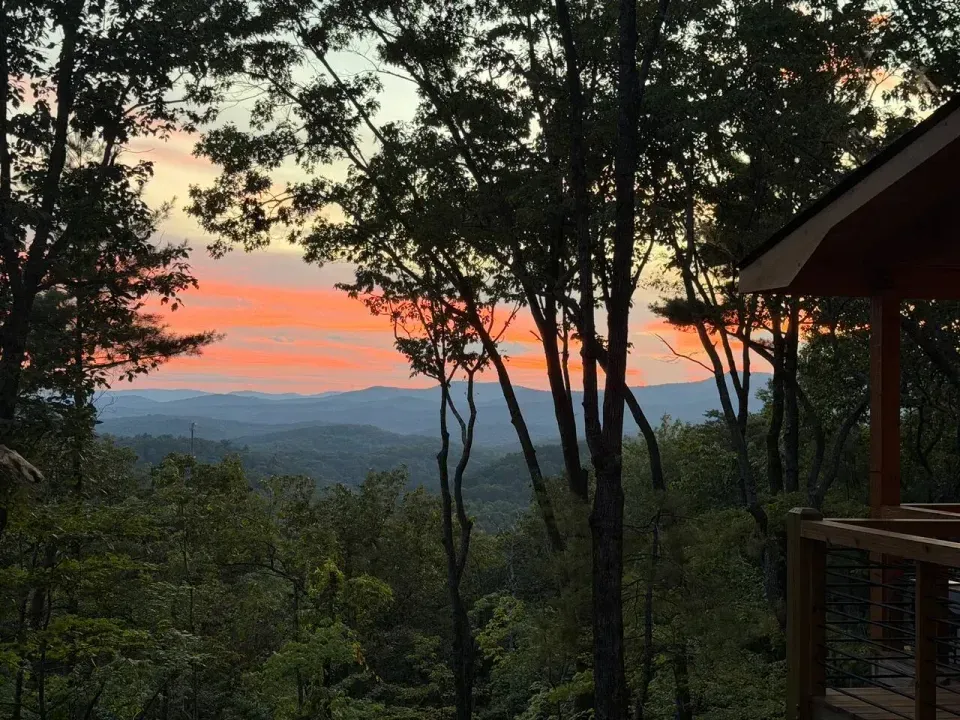 Sunset over layered Blue Ridge Mountain ridgelines, seen through the trees from the deck at Amber Ridge Retreat in Cherry Log, GA