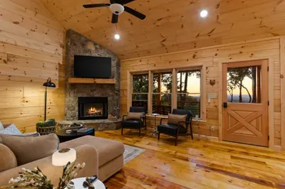 Cozy cabin living room with stone fireplace and scenic wooded views. Large QLED TV, Koala Sleeper Sofa