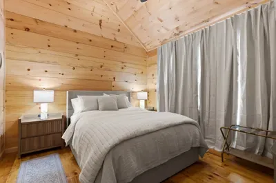 Cozy wood-lined bedroom with plush bed and serene cabin charm. Primary Bedroom with En Suite. Brooklyn Bed Co bed, hypoallergenic luxury linens.