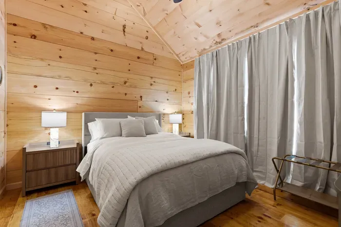 Cozy wood-lined bedroom with plush bed and serene cabin charm. Primary Bedroom with En Suite. Brooklyn Bed Co bed, hypoallergenic luxury linens.