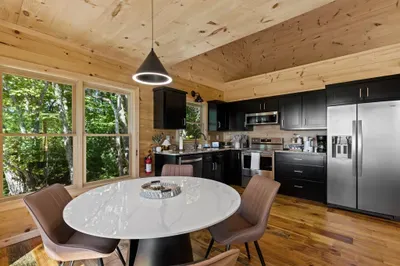 Modern cabin kitchen with forest views, sleek finishes, and cozy dining