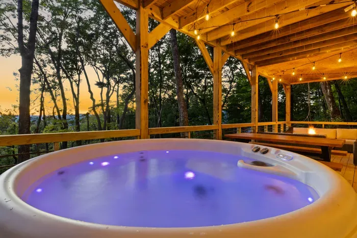 Relax in the hot tub under string lights on a serene wooded deck