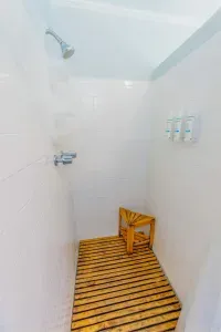 Walk in shower with mounted dispensers and a wood stool providing guests with essential bathing amenities in a simple layout.