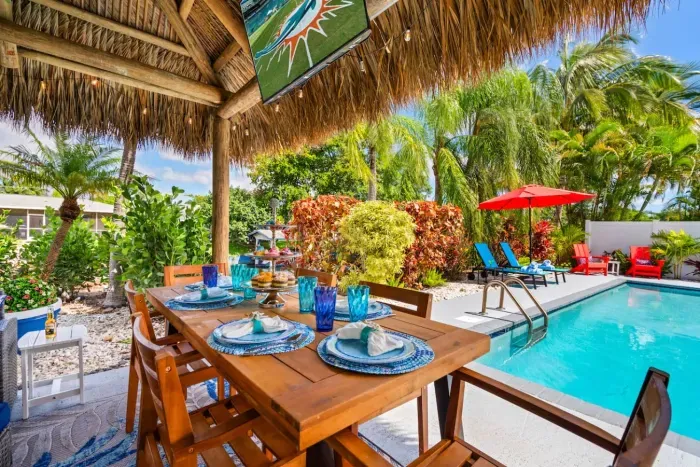 The tiki hut with bar, furniture, seating, dining table, and 55" smart TV is your own outdoor lounge, perfect for game days, evening cocktails, and al fresco meals.