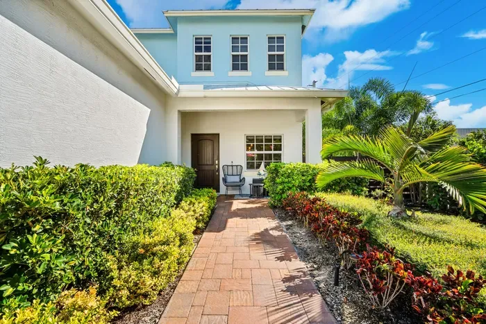 Front view of this newly built home with tropical landscaping, decorative blue glass, and accenting palm trees.